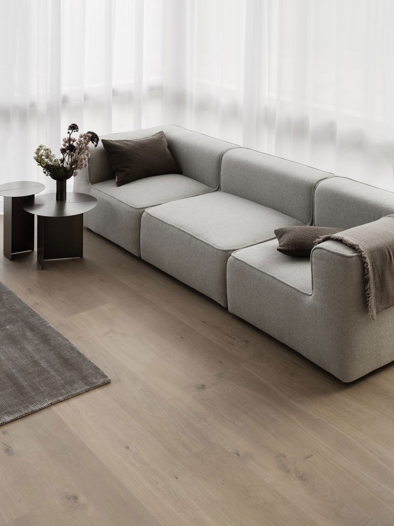 Modern gray sofa with cushions and side tables in a bright, minimalistic living room.