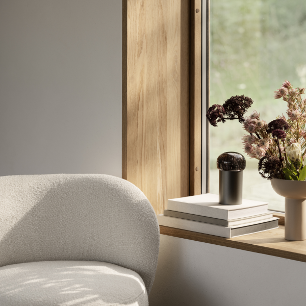Gemütliches Interieur mit einem plüschigen Stuhl, Büchern und einer Vase mit Blumen neben einem sonnigen Fenster.