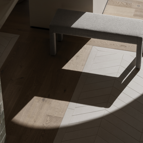 Stylische graue Bank, die Schatten auf einem modernen Holzboden mit Fischgrätenmustern wirft.