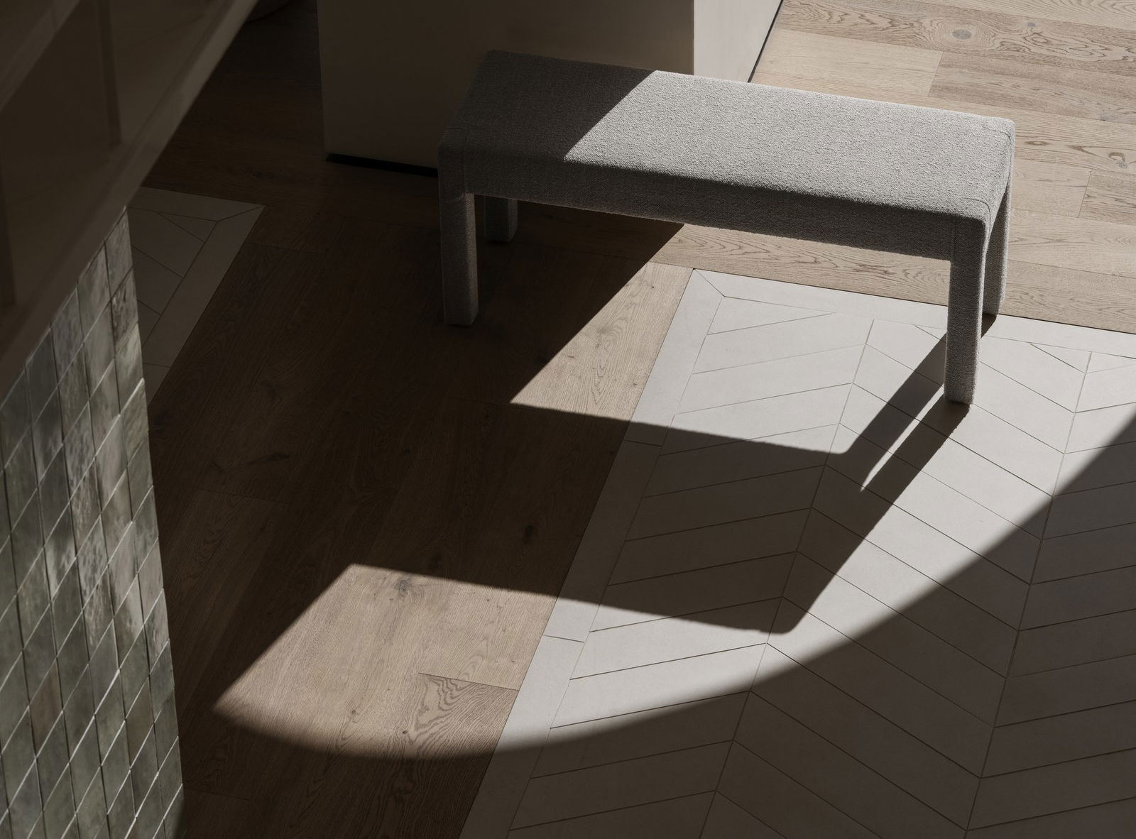Stylische graue Bank, die Schatten auf einem modernen Holzboden mit Fischgrätenmustern wirft.