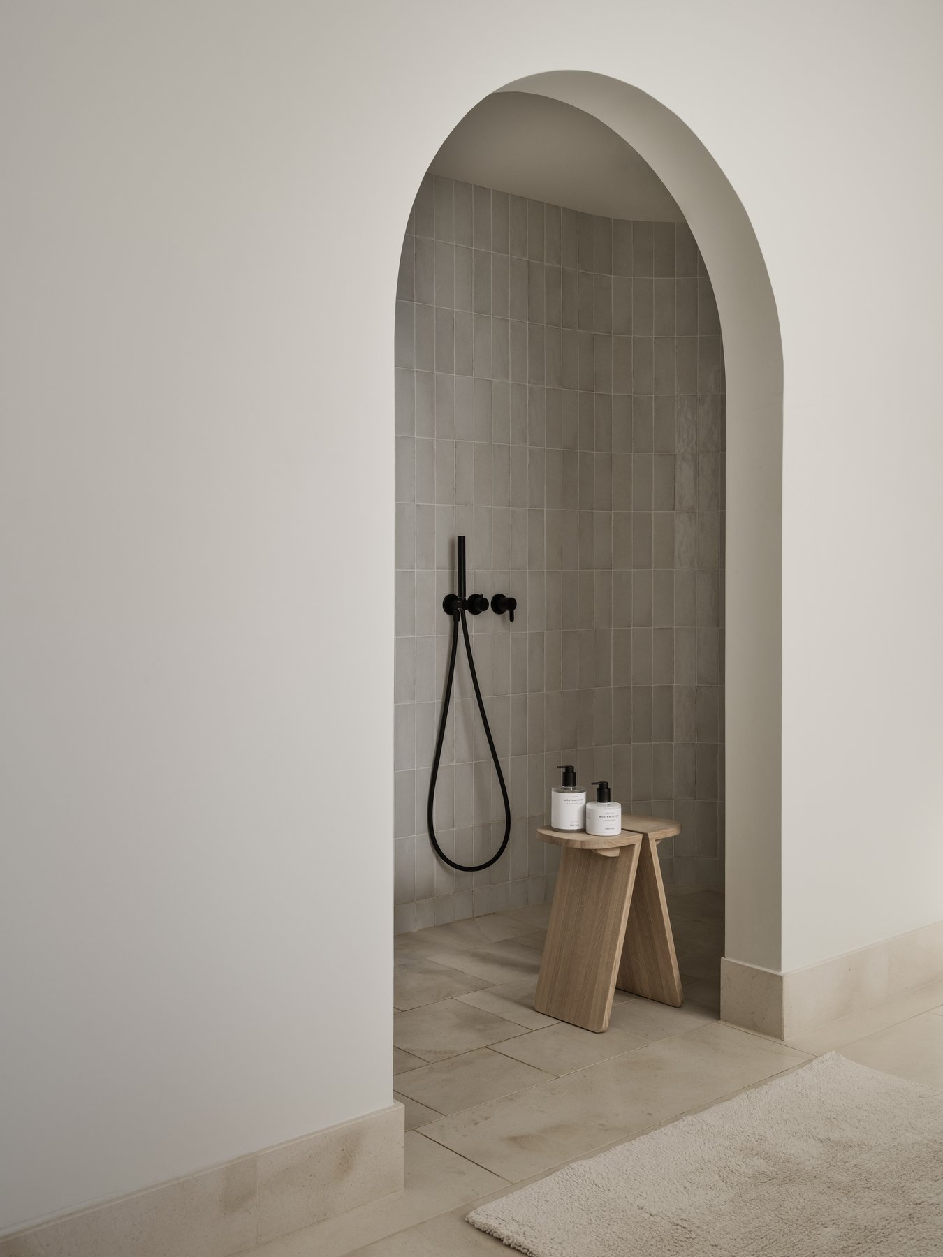 Moderner minimalistischer Duschbereich mit grauen Fliesen und einem Holzstuhl für Toilettenartikel.
