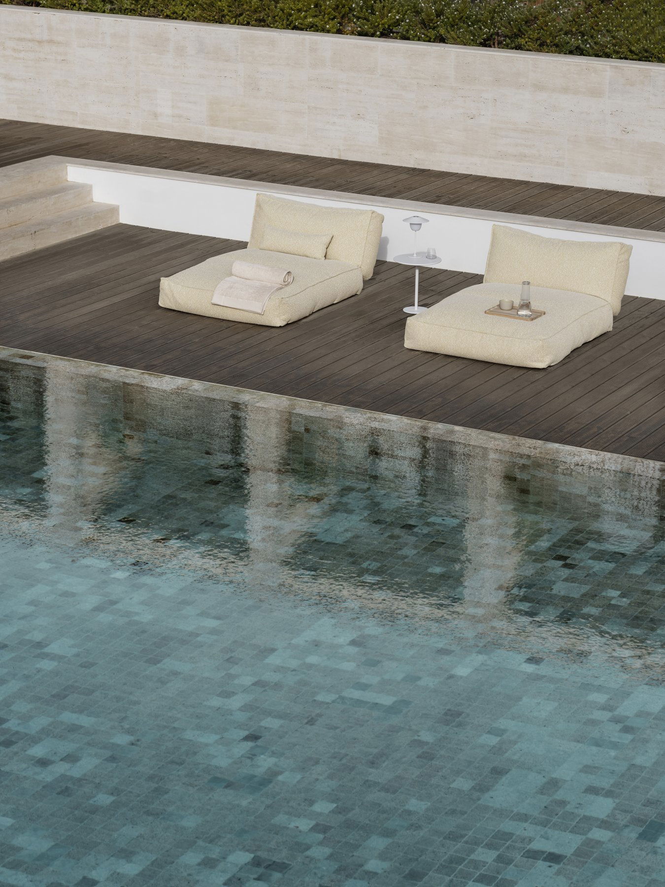 Luxurious poolside loungers beside a tranquil water surface for relaxation.