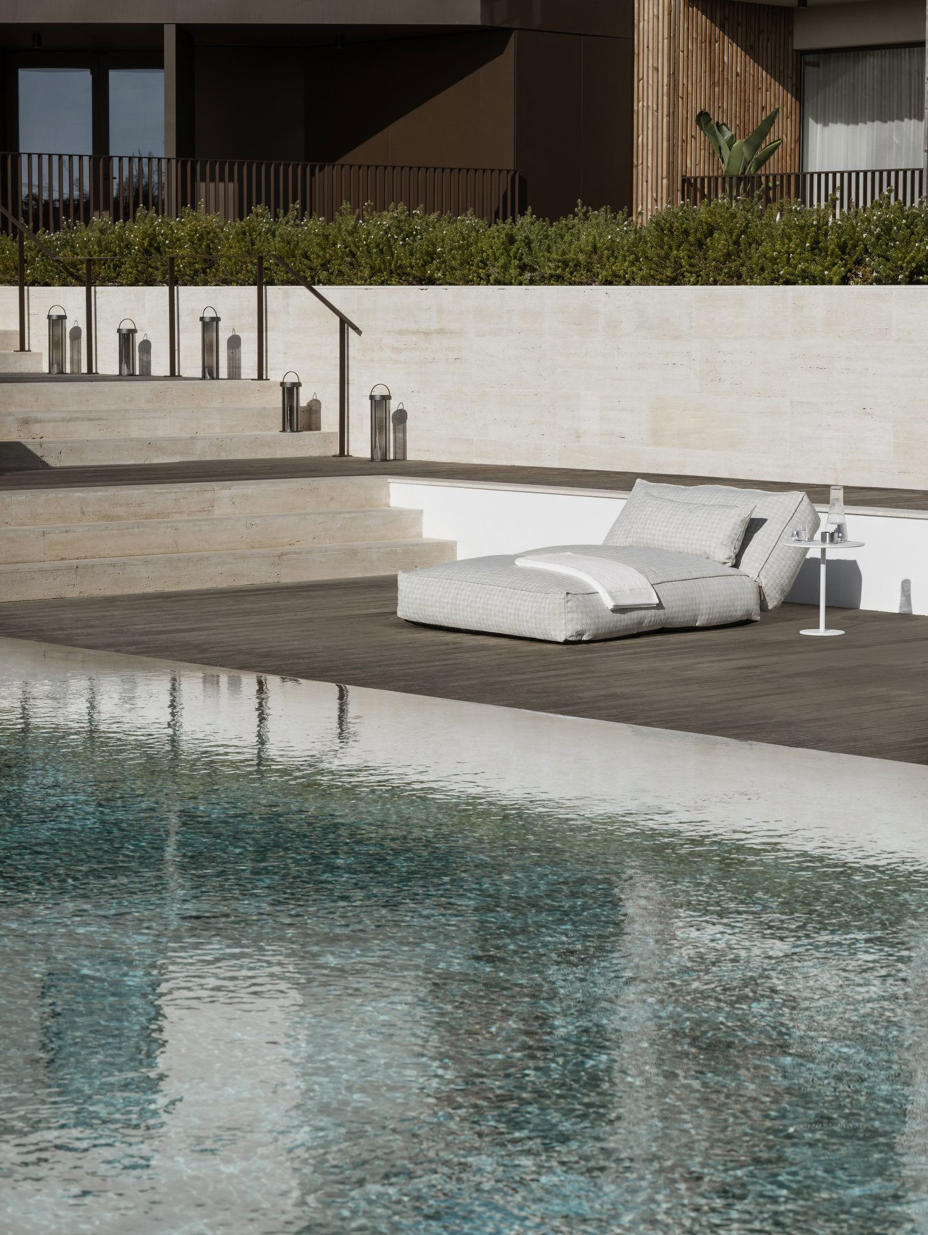 Lounge chair by a serene poolside with modern steps and lush greenery in the background.