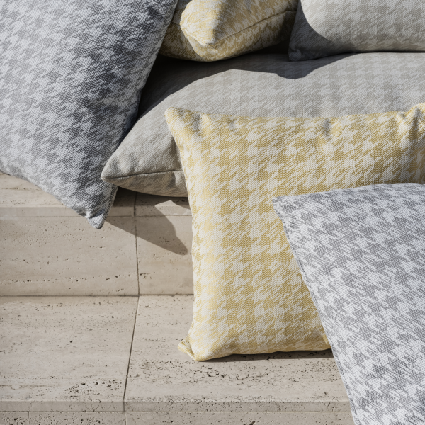 Cozy houndstooth patterned pillows in gray, yellow, and white stacked on a stone surface.