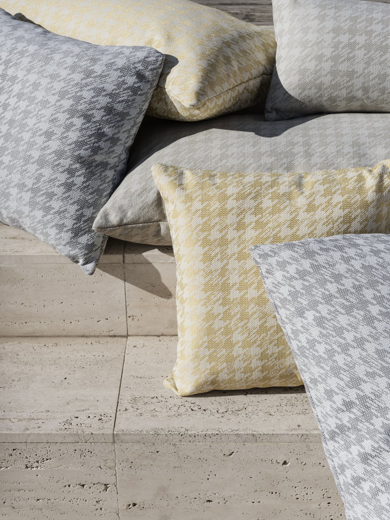 Cozy houndstooth patterned pillows in gray, yellow, and white stacked on a stone surface.
