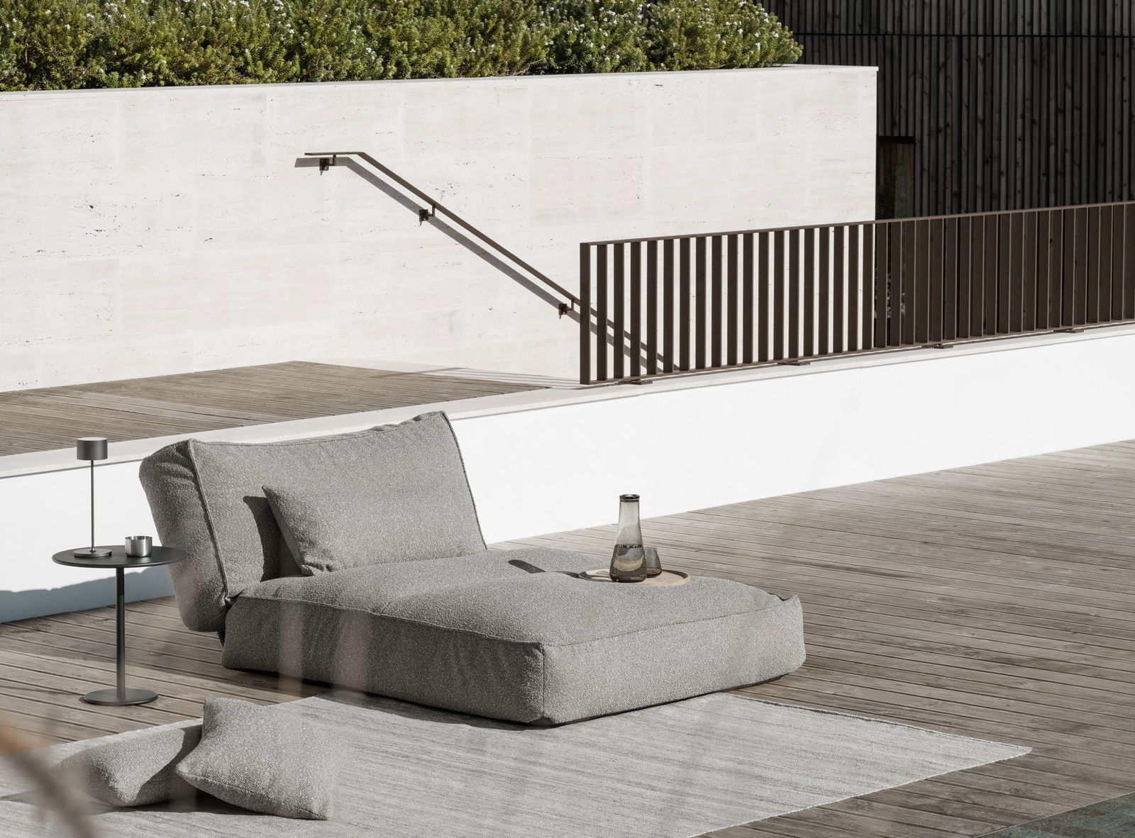 Modern outdoor lounge area featuring a stylish gray chaise and glass water bottle.