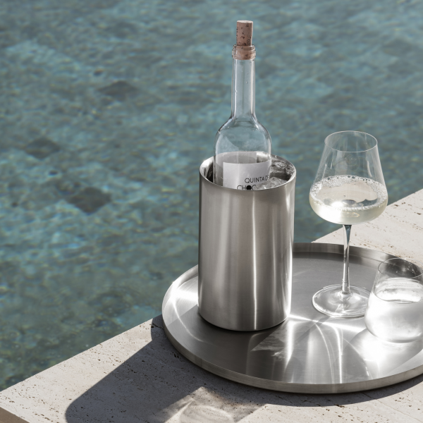 Chic wine bottle and glass on a tray beside a serene swimming pool.