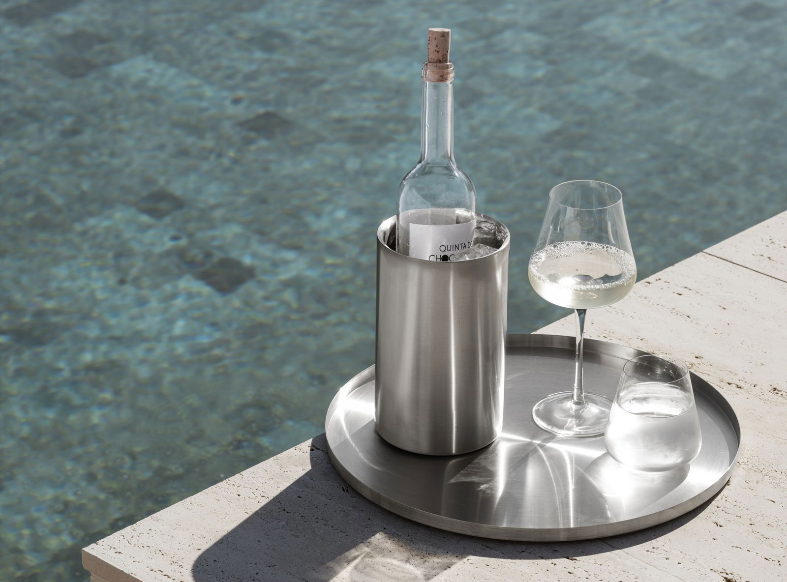 Chic wine bottle and glass on a tray beside a serene swimming pool.