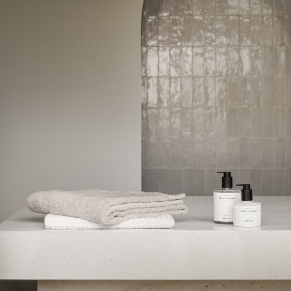 Neutrale Badezimmerdekoration mit weichen Handtüchern und stylischen Hautpflegeprodukten auf einer eleganten Arbeitsplatte.