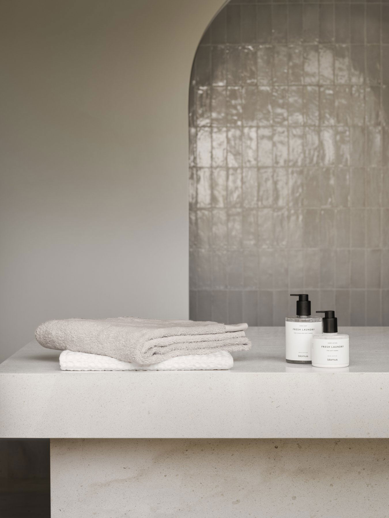 Neutrale Badezimmerdekoration mit weichen Handtüchern und stylischen Hautpflegeprodukten auf einer eleganten Arbeitsplatte.