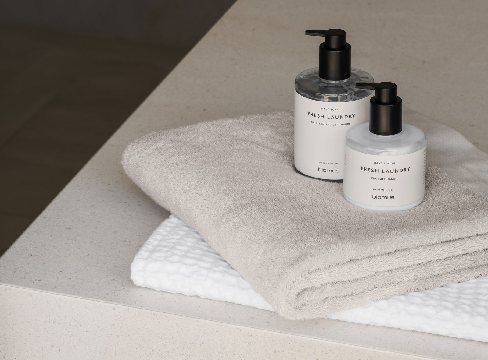 Bottles of fresh laundry soap beside soft towels on a clean countertop.