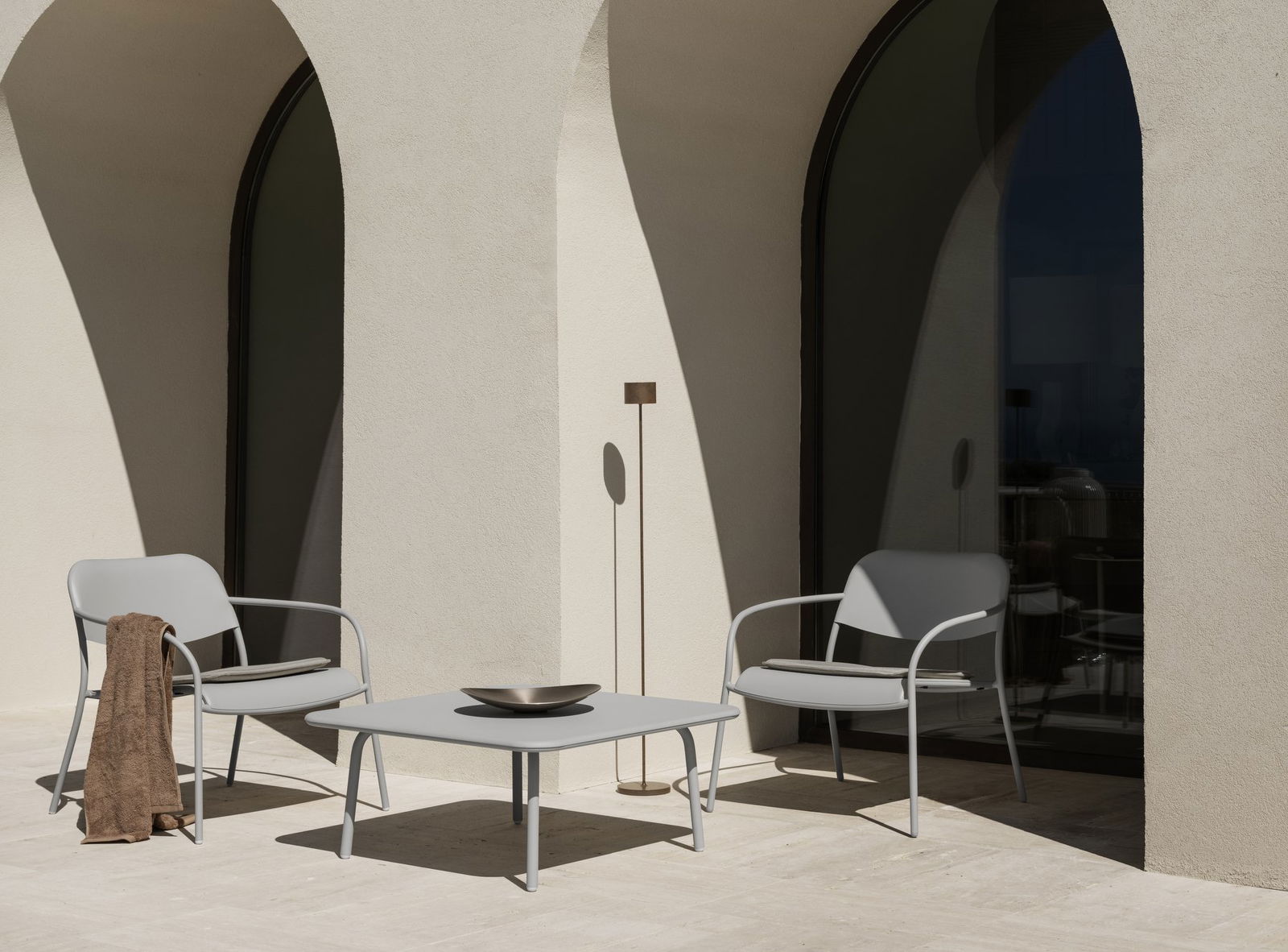 Minimalist outdoor patio with elegant chairs and a stylish table near arched windows.