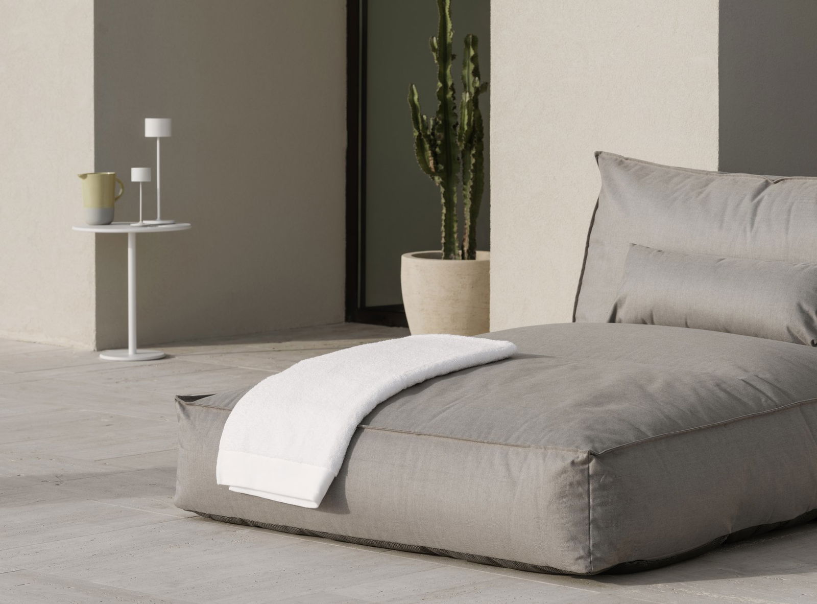 Cozy outdoor seating area with a gray cushion and a white towel beside a potted cactus.