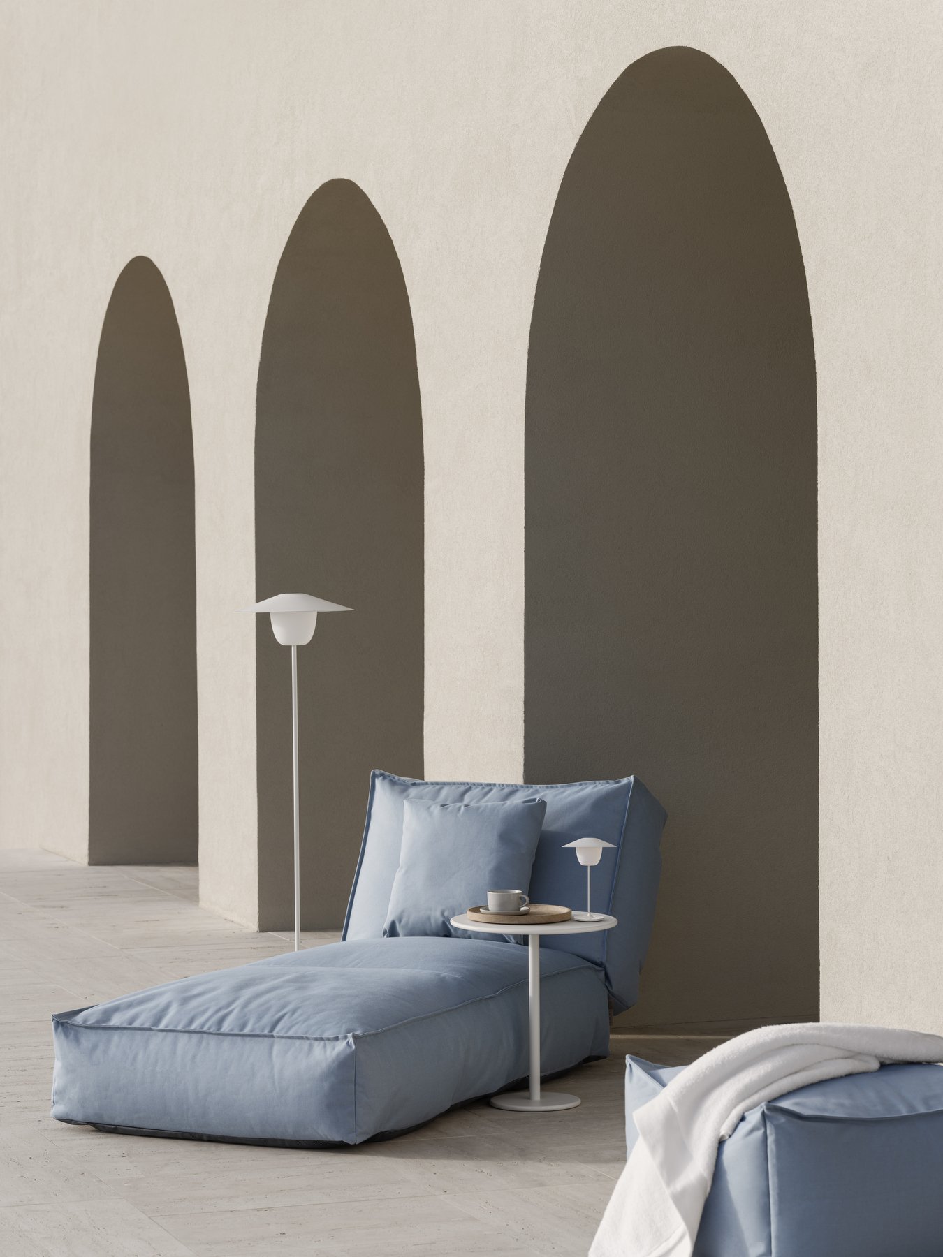 Moderner Außen-Loungebereich mit blauen Kissen und minimalistischer Dekoration unter gewölbter Architektur.