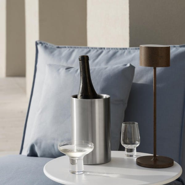 Stylish table setting with champagne, glasses, and a modern lamp on cozy blue pillows.