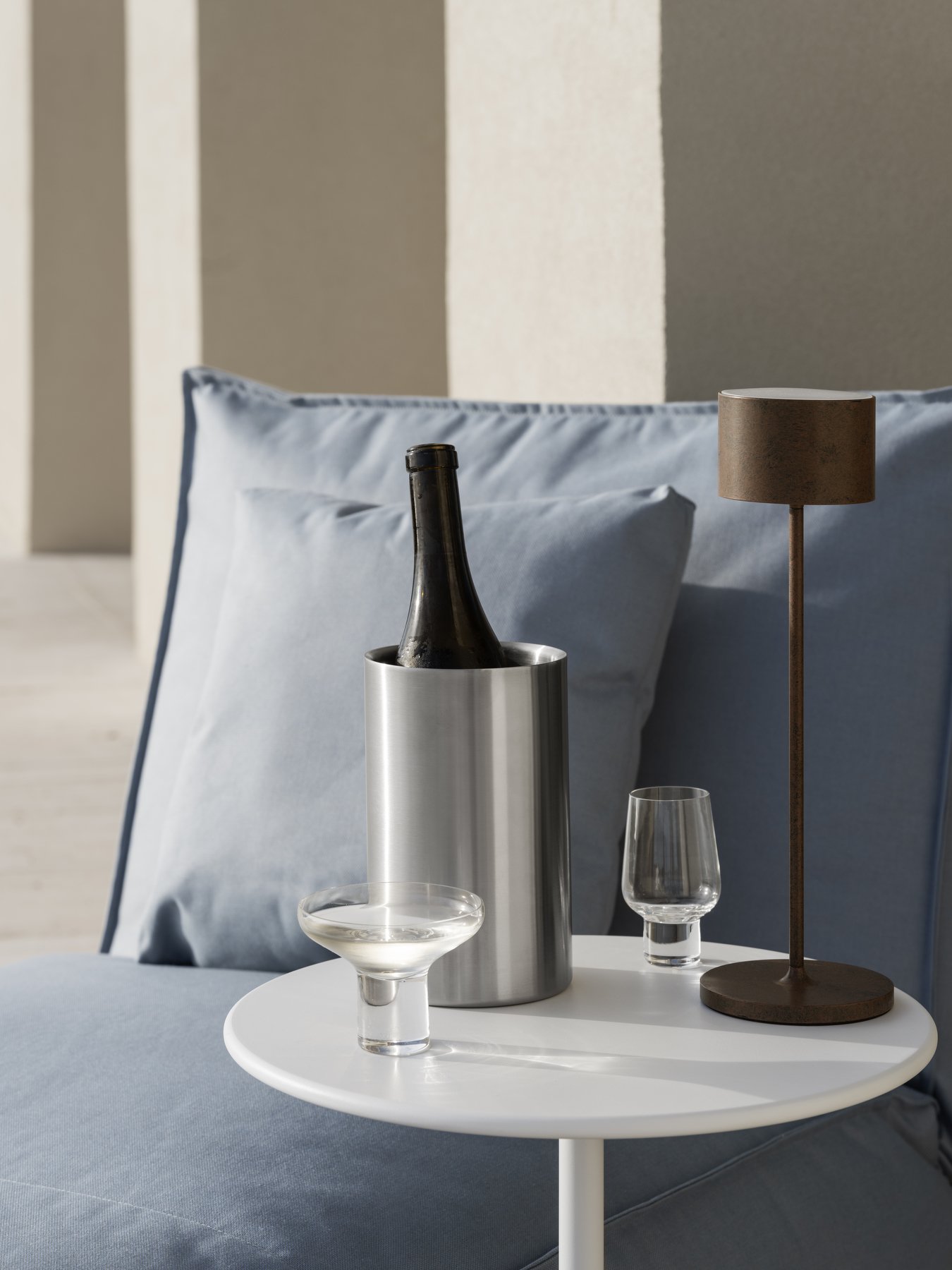 Stylish table setting with champagne, glasses, and a modern lamp on cozy blue pillows.
