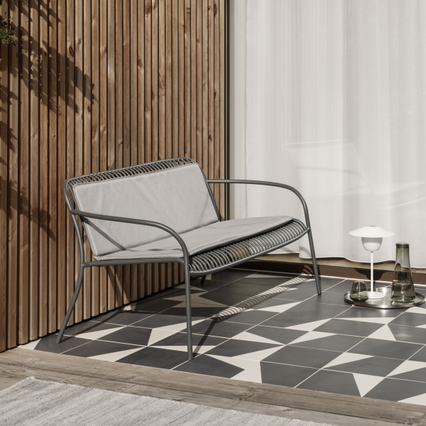 Moderner Outdoor-Sofa mit grauem Stoff auf einem stilvollen gemusterten Terrassenboden.