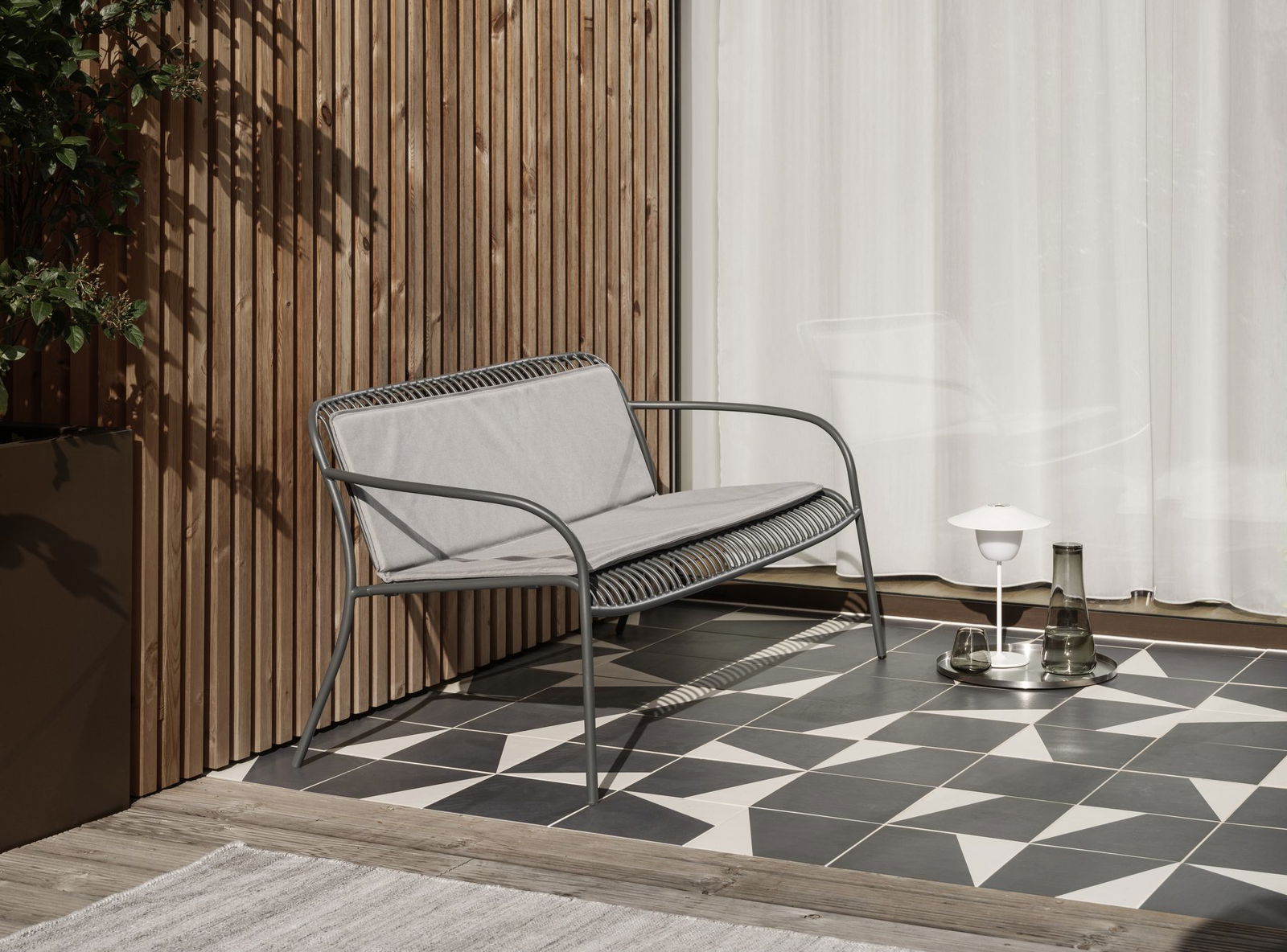 Moderner Outdoor-Sofa mit grauem Stoff auf einem stilvollen gemusterten Terrassenboden.