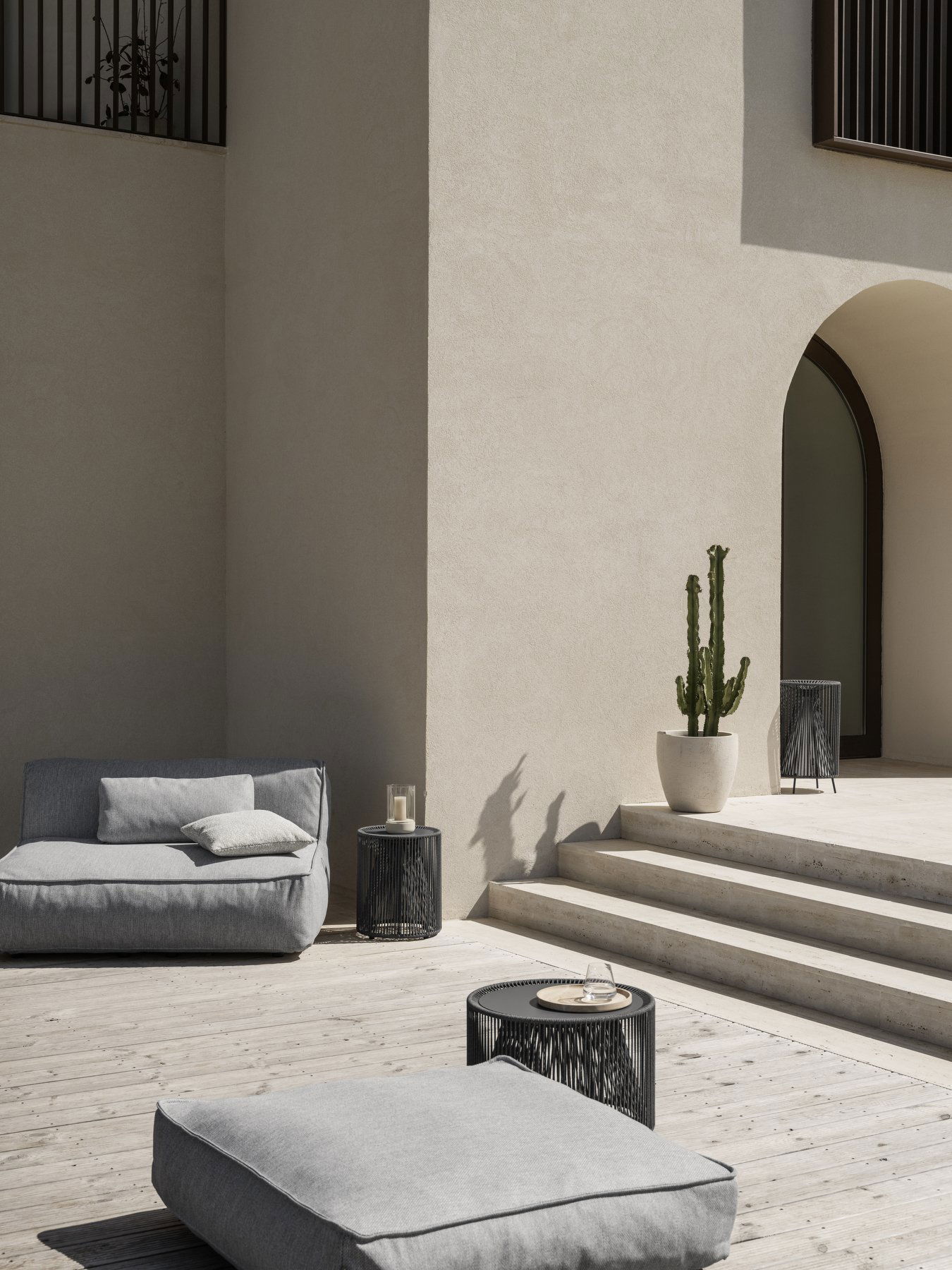 Moderner Outdoor-Patio mit einem minimalistischen Sofa, stilvollen Tischen und einem großen Kaktus.