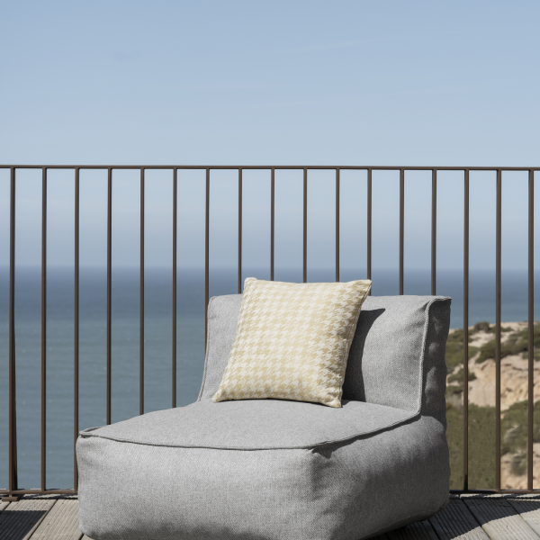 Cozy gray lounge chair with a decorative pillow overlooking a serene ocean view.