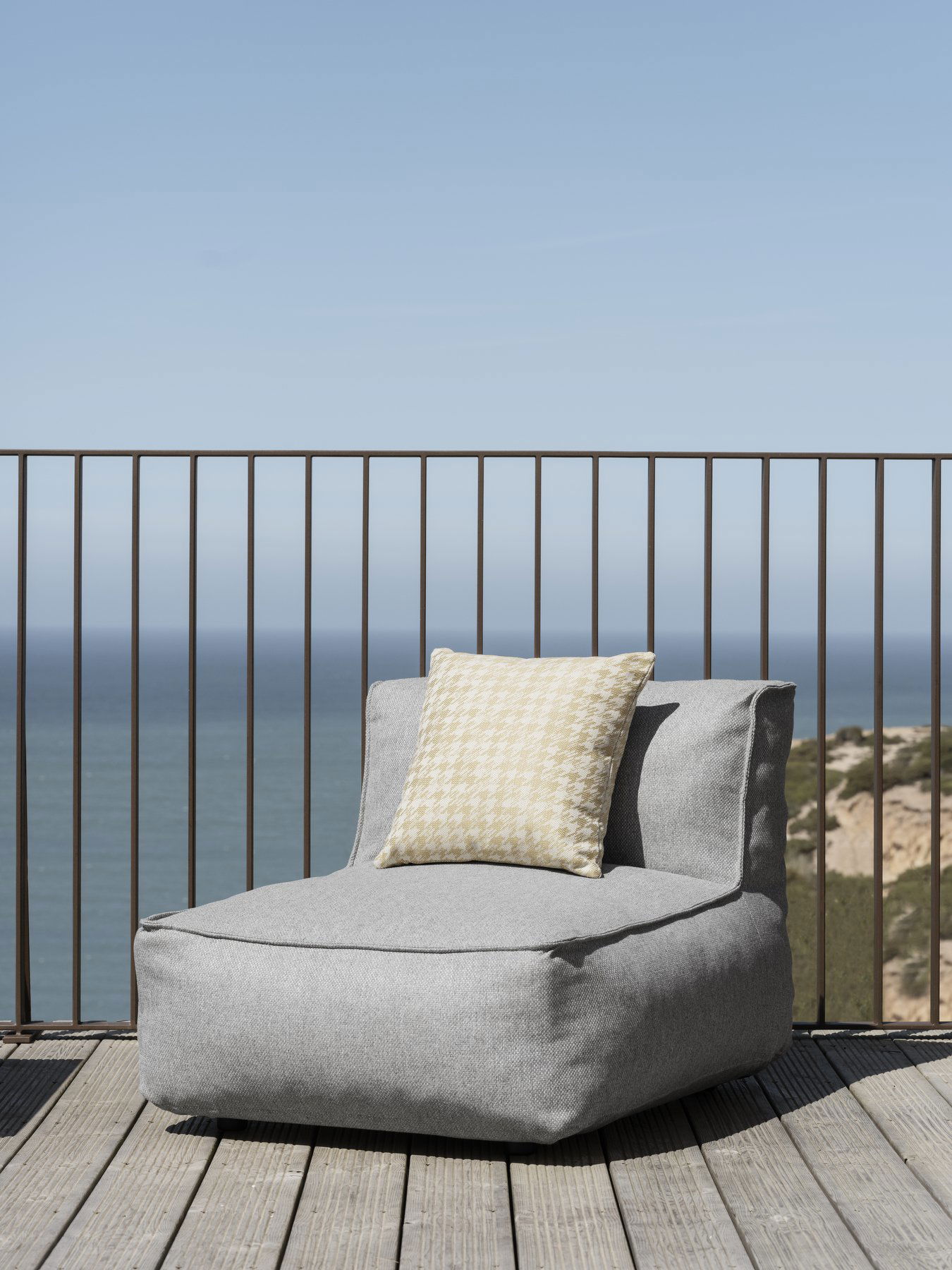 Cozy gray lounge chair with a decorative pillow overlooking a serene ocean view.