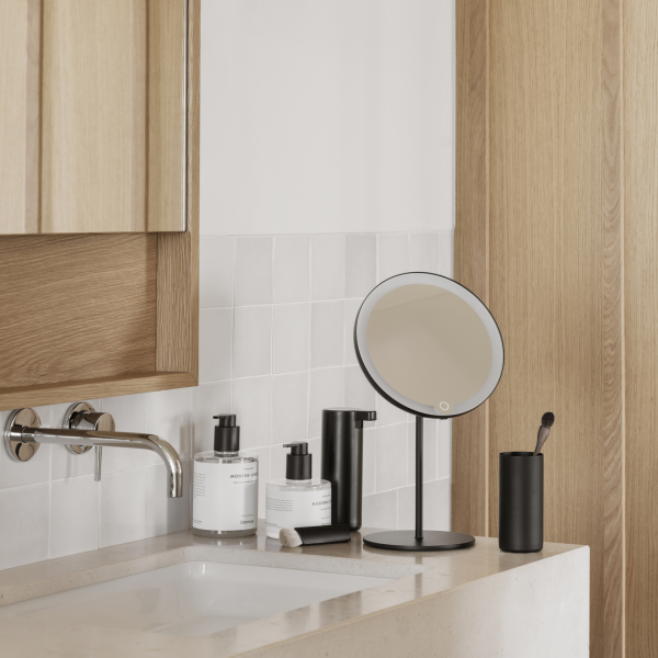 Modern bathroom setup with a round mirror, skincare products, and stylish fixtures.