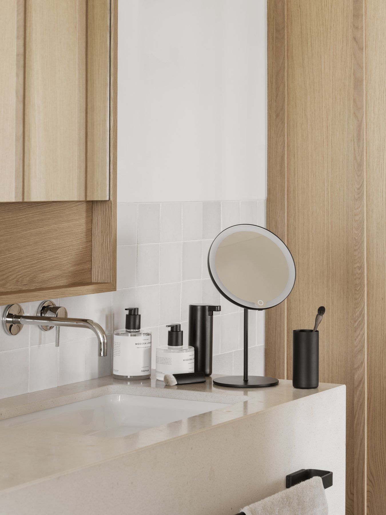 Modern bathroom setup with a round mirror, skincare products, and stylish fixtures.