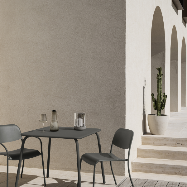 Modern outdoor dining setup with chairs, table, and potted cactus against a textured wall.