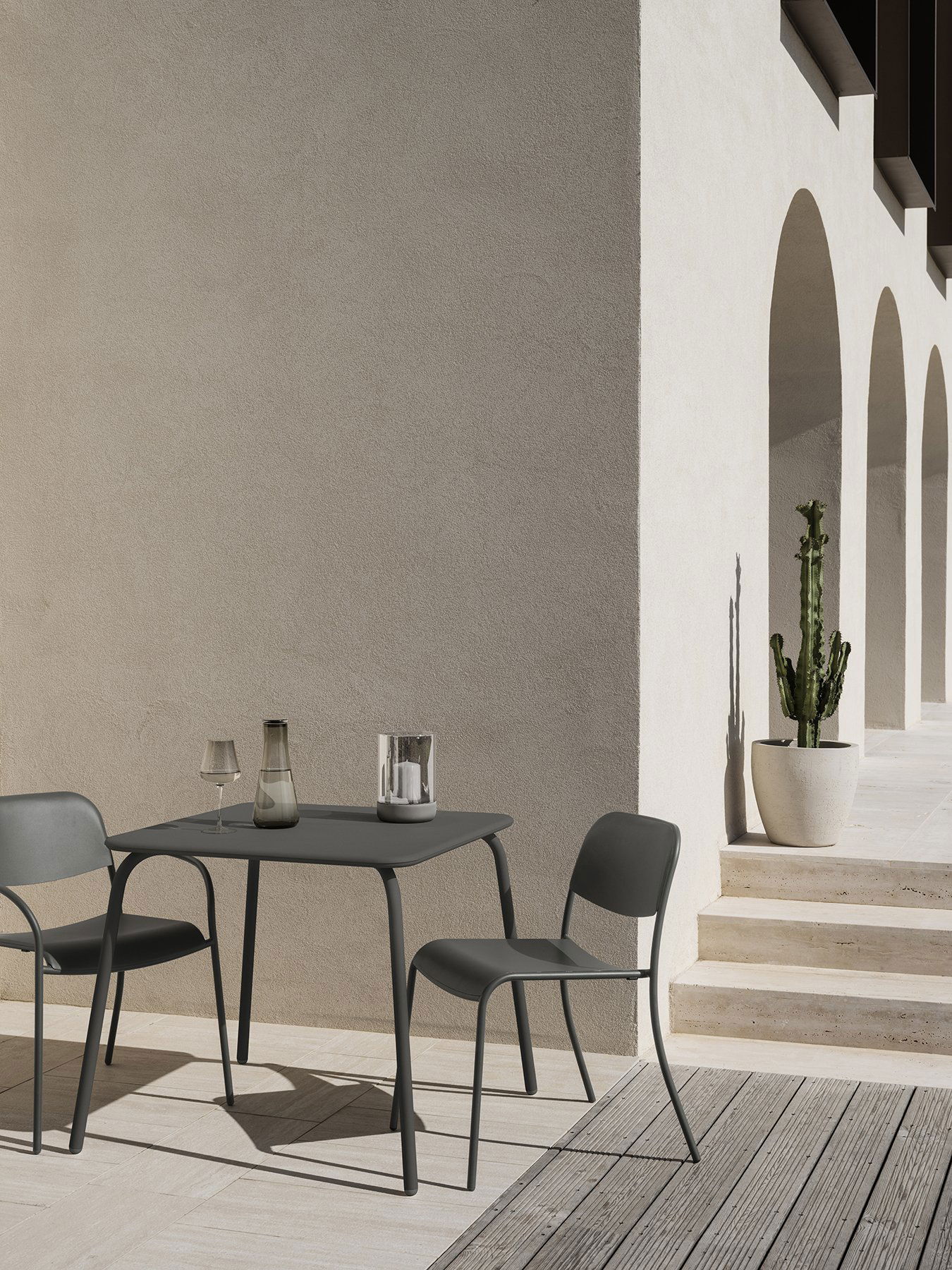 Modern outdoor dining setup with chairs, table, and potted cactus against a textured wall.