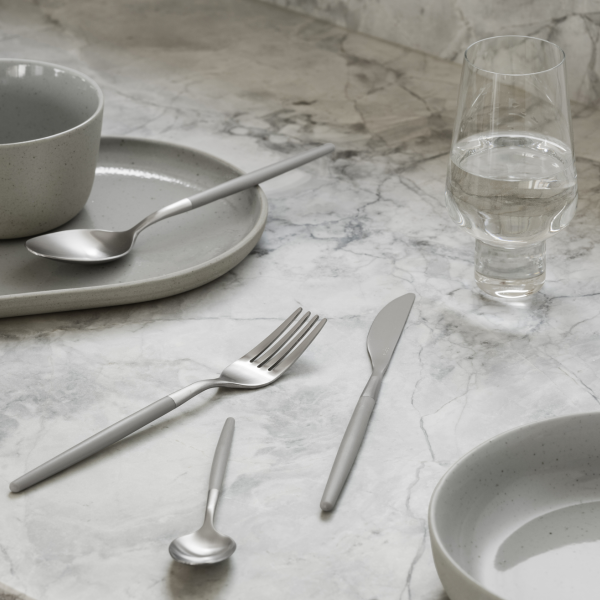 Elegant table setting with modern grey dishware and stainless steel utensils on marble surface.