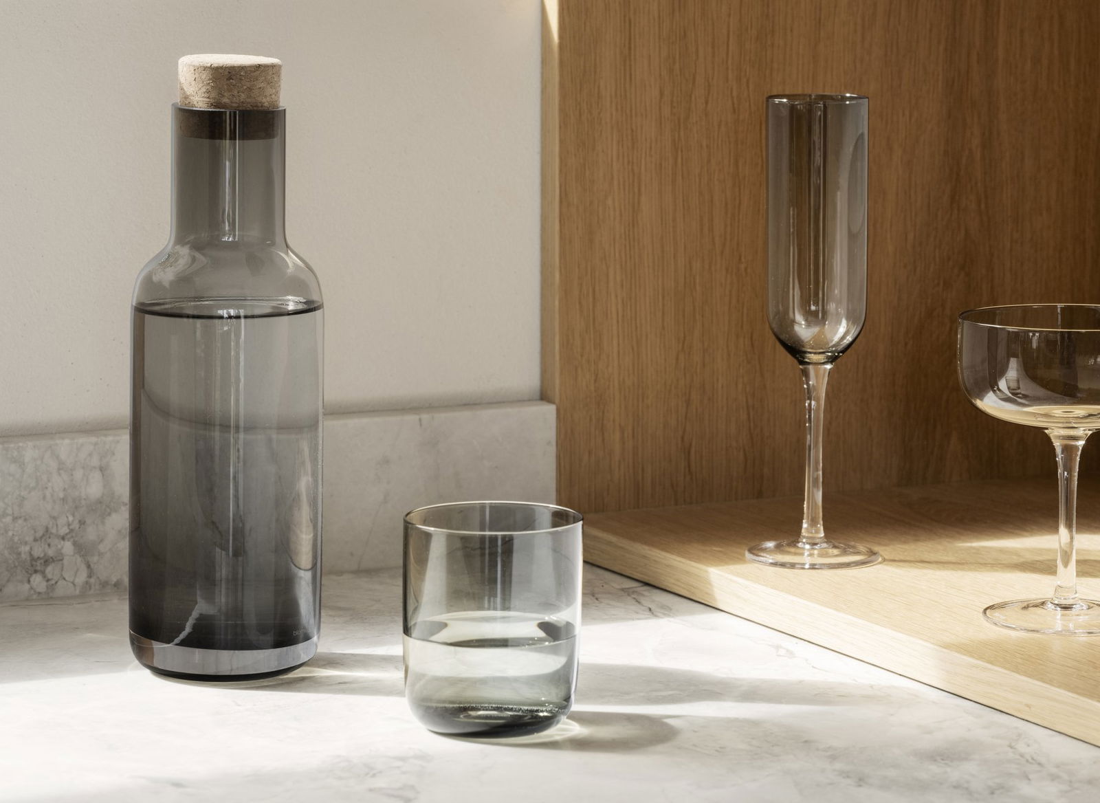 Elegante Glaswarenanordnung mit einer grauen Flasche und stilvollen Trinkgläsern auf einer Marmoroberfläche.