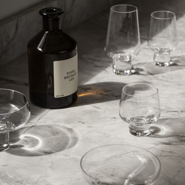 Elegantes Glasgeschirr und eine Flasche Gin auf einer marmorierten Küchenarbeitsplatte, die verspielte Schatten werfen.