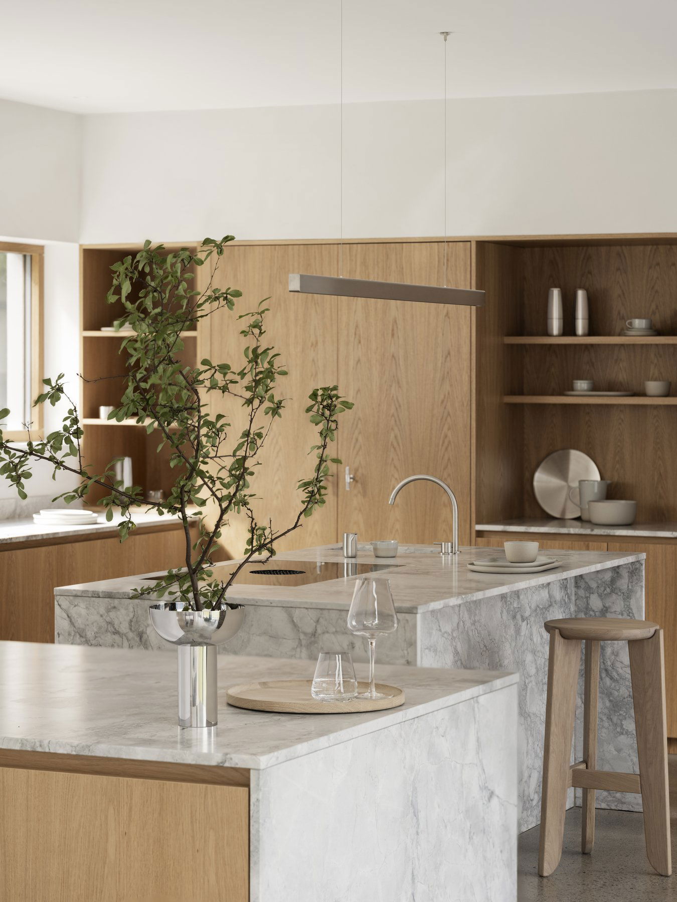 Moderne Küche mit Marmorinsel, Holzmöbeln und einer minimalistischen dekorativen Pflanze.