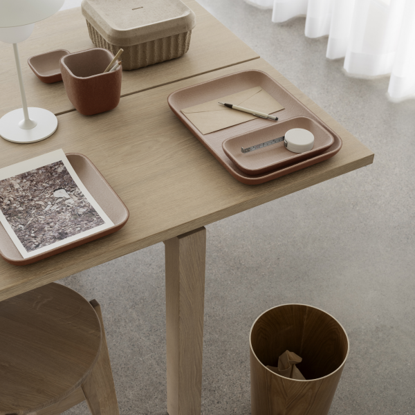 Minimalistischer Arbeitsplatz mit einem Holztisch, auf dem Tabletts, Büromaterial und dekorative Elemente liegen.
