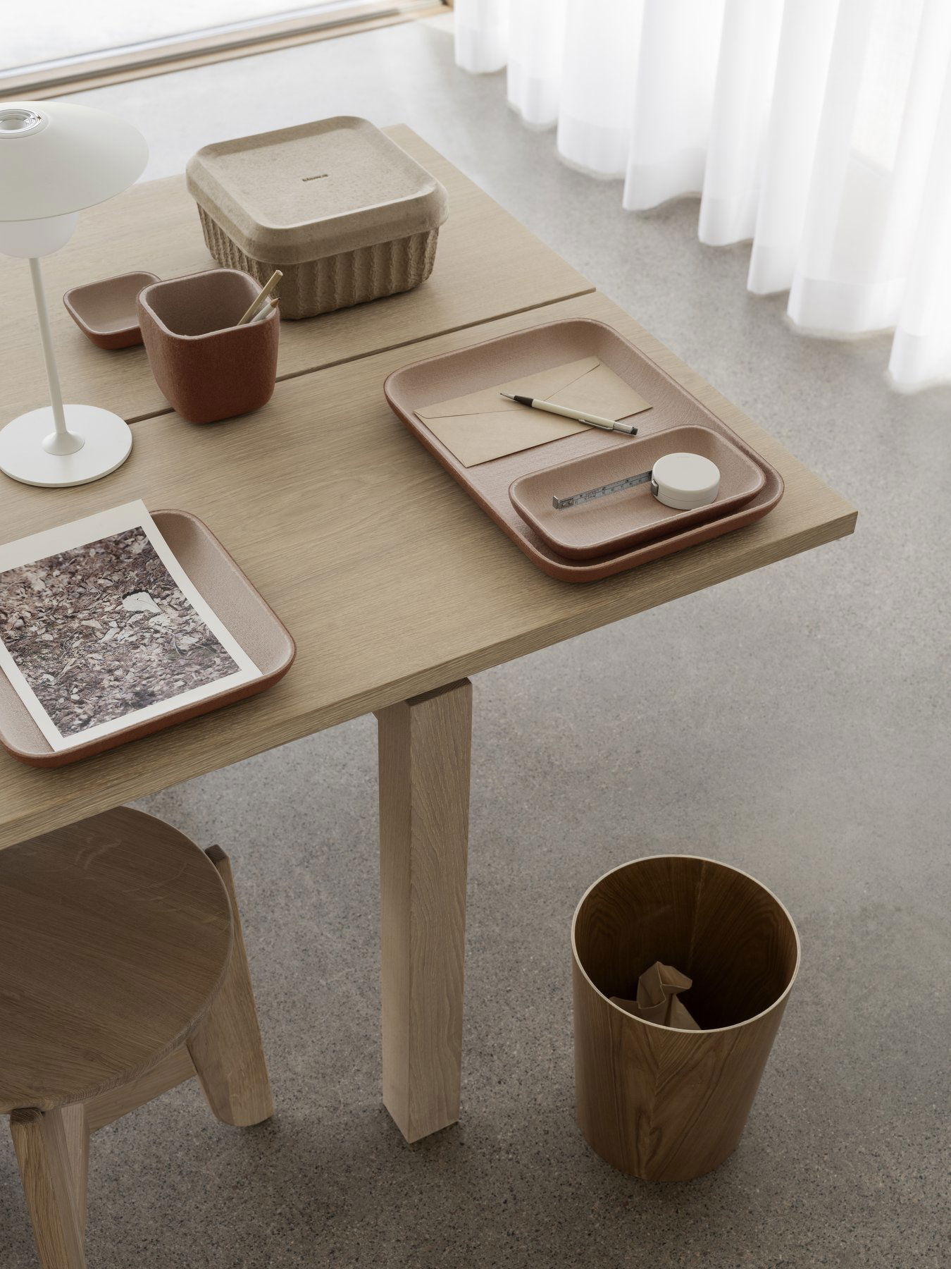Minimalistischer Arbeitsplatz mit einem Holztisch, auf dem Tabletts, Büromaterial und dekorative Elemente liegen.