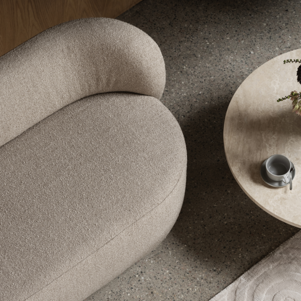 Elegantes beiges Sofa neben einem runden Couchtisch mit Blumen und einer Tasse platziert.