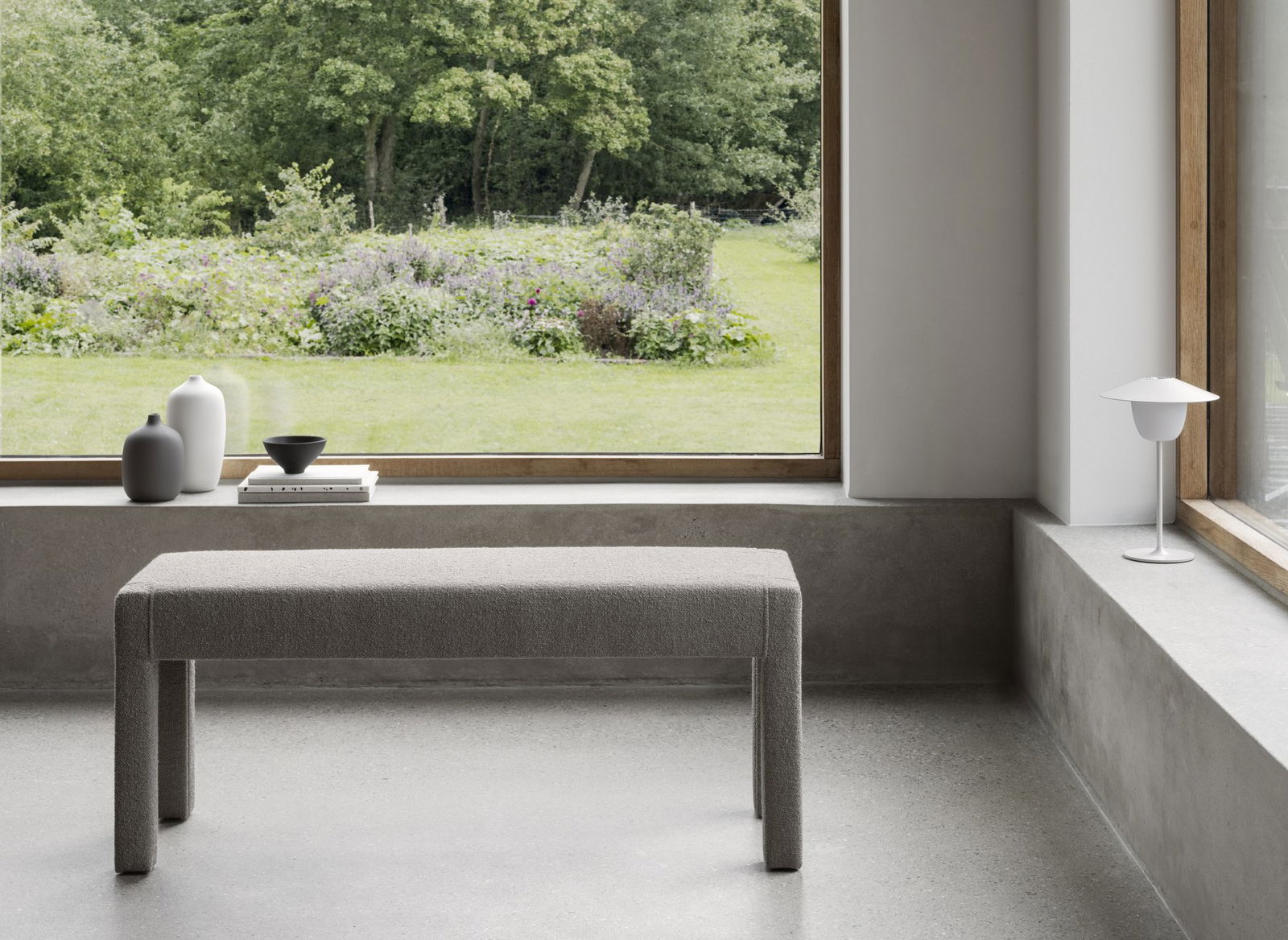 Moderner minimalistischer Innenraum mit einer grauen Bank und Blick auf den Garten durch ein großes Fenster.