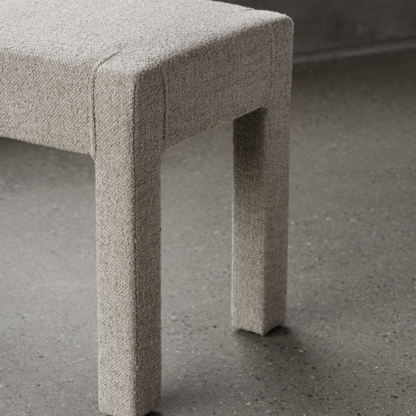 Moderne gepolsterte Bank mit strukturiertem Stoff und minimalistischem Design auf einem Betonboden.