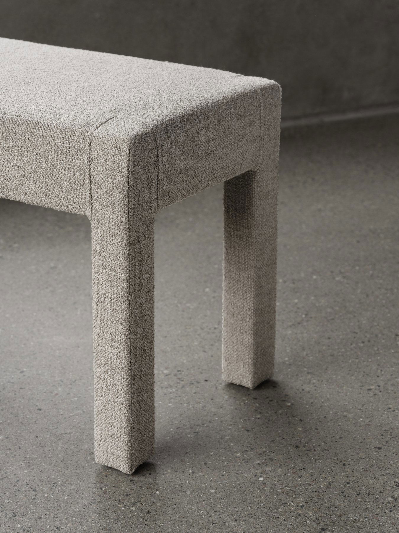 Moderne gepolsterte Bank mit strukturiertem Stoff und minimalistischem Design auf einem Betonboden.