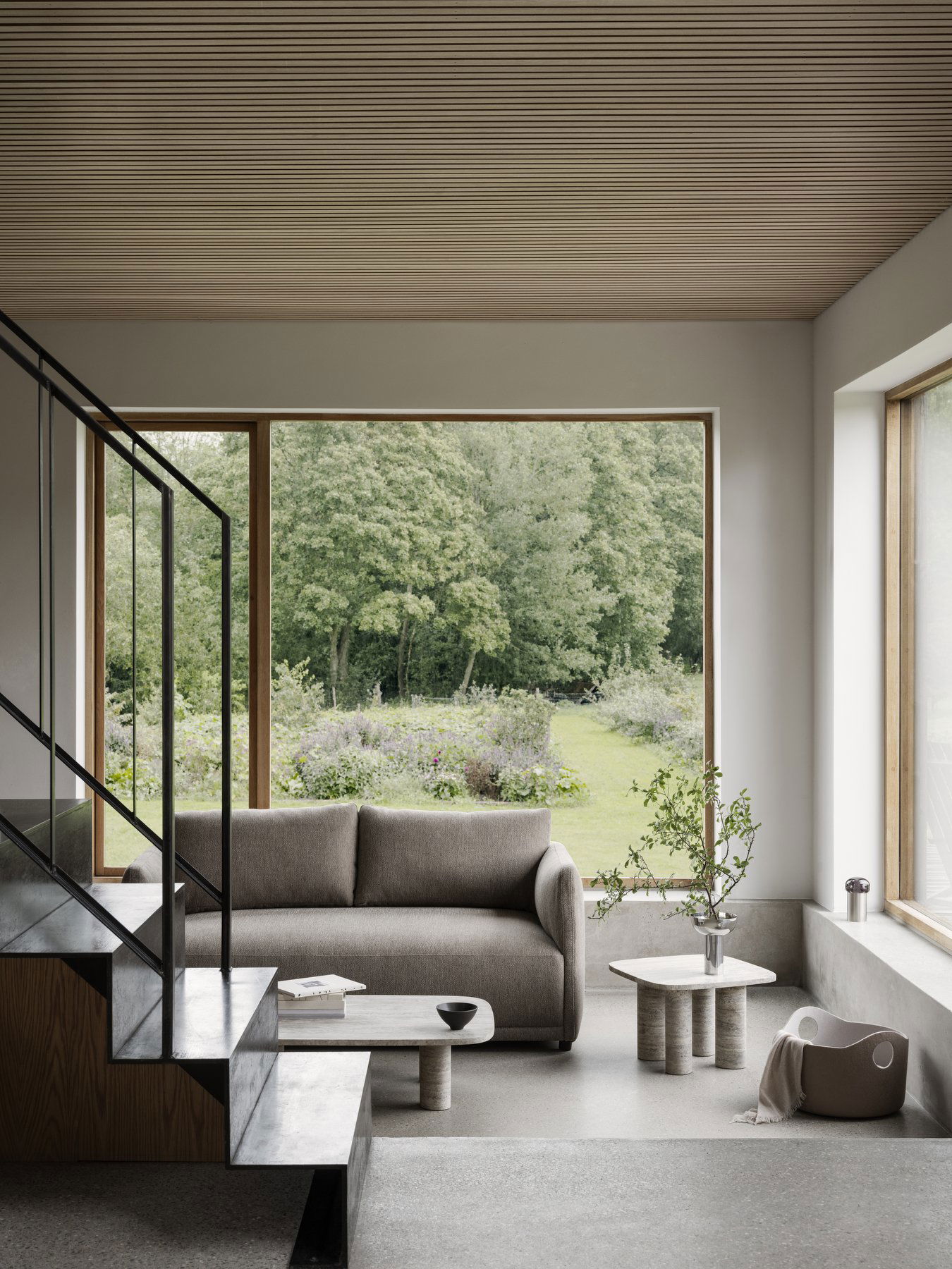 Moderner Wohnraum mit einem gemütlichen Sofa und einem weiten Blick auf einen üppigen Garten draußen.