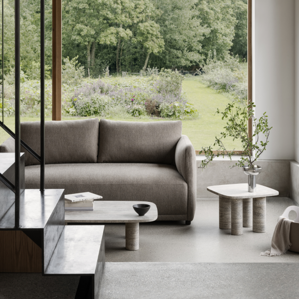 Moderner Wohnraum mit einem grauen Sofa, minimalistischen Möbeln und Blick auf eine üppig grüne Außensicht.