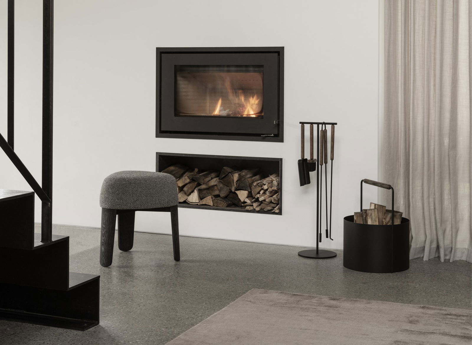 Modern living room with a black wall fireplace, log storage, and stylish seating.