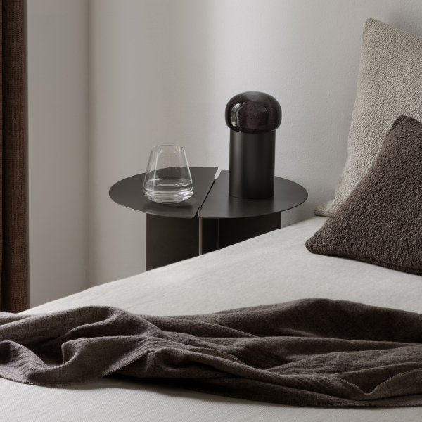 Eleganter Nachttisch mit einem Glas Wasser und einer modernen Lampe in einem minimalistischen Schlafzimmer.