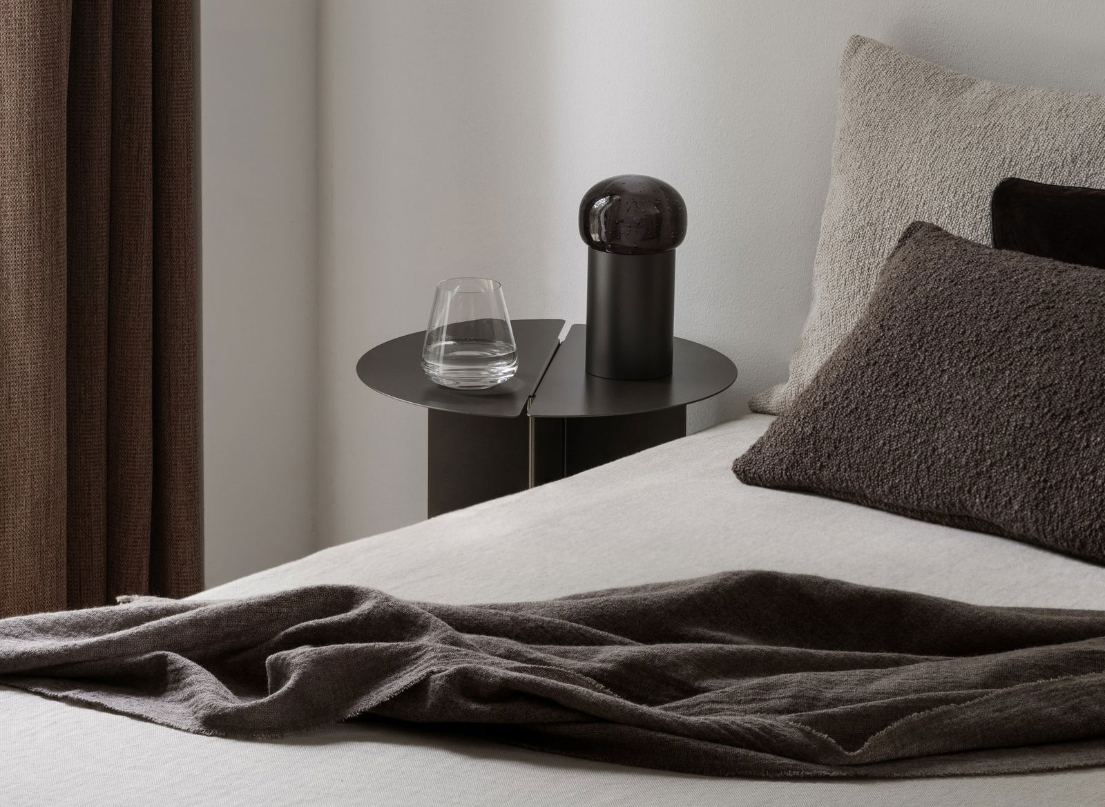 Eleganter Nachttisch mit einem Glas Wasser und einer modernen Lampe in einem minimalistischen Schlafzimmer.
