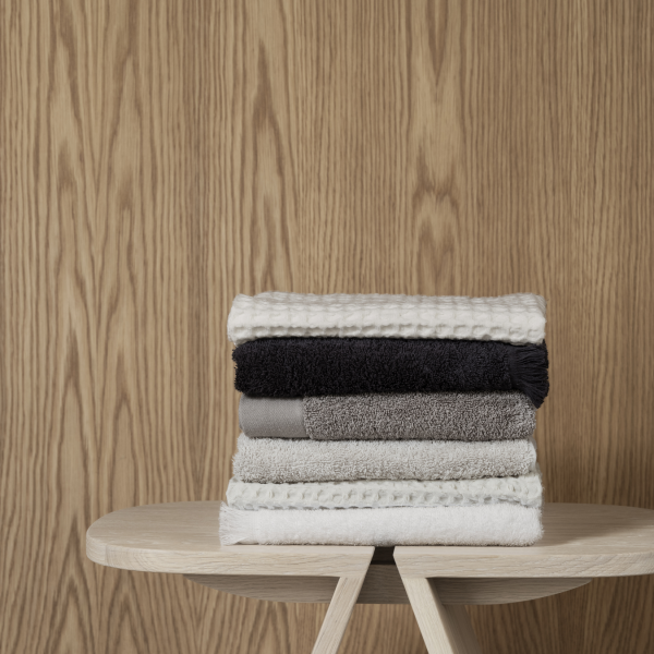 Stack of soft, textured towels in neutral colors atop a wooden table against a rustic background.