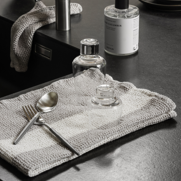 Elegant kitchen scene featuring glass bottles, silver utensils, and a textured cloth.