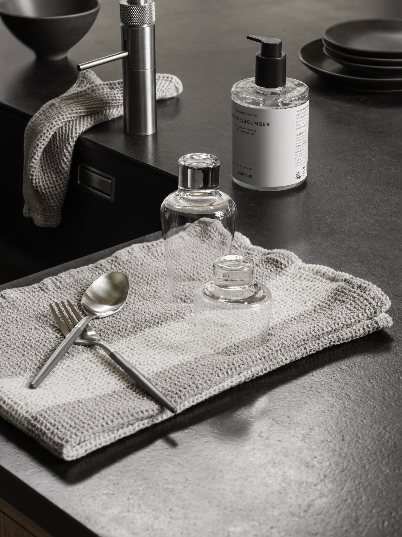 Elegant kitchen scene featuring glass bottles, silver utensils, and a textured cloth.