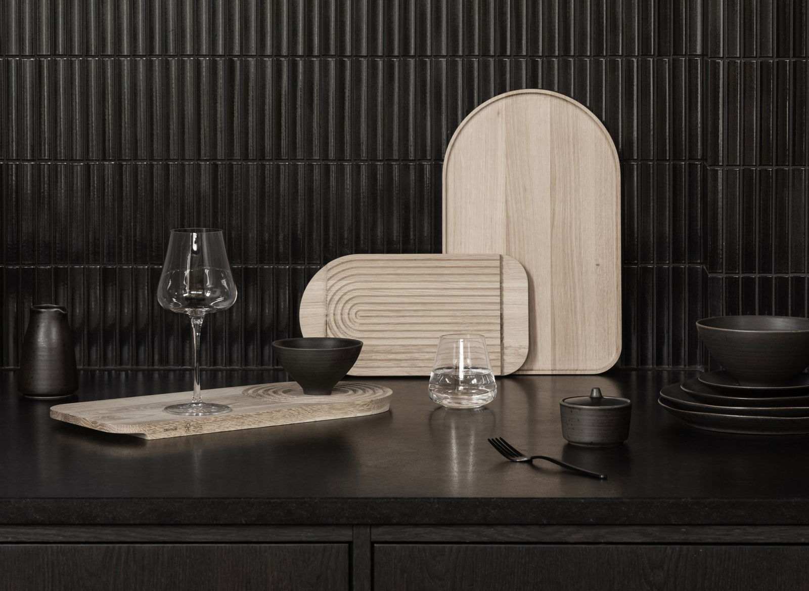 Elegante Holzservierplatten und Glaswaren auf einer dunklen Küchenarbeitsplatte.