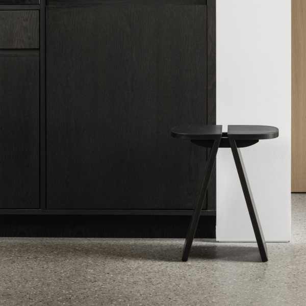 Minimalist black wooden stool beside a sleek, modern kitchen cabinet.