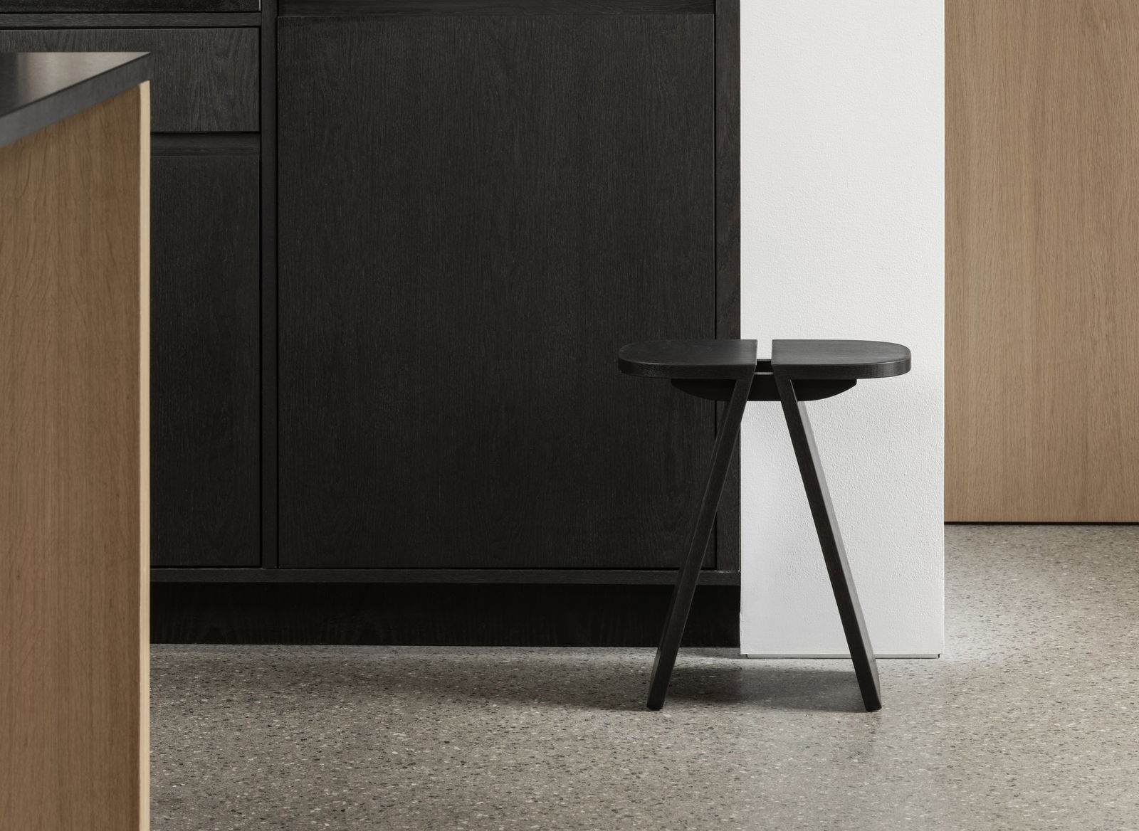 Minimalist black wooden stool beside a sleek, modern kitchen cabinet.